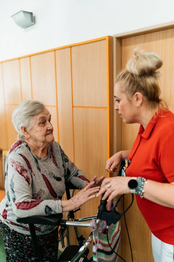 Pflegerin lächelt mit älterer Patientin zu Hause
